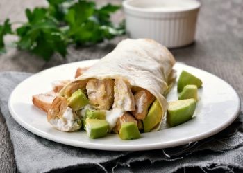 primo piano di un piatto bianco sul tavolo con burrito di pollo e avocado