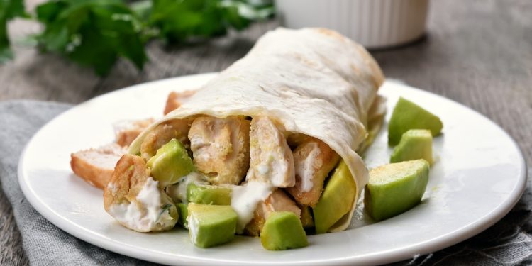 primo piano di un piatto bianco sul tavolo con burrito di pollo e avocado