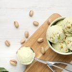 Gelato al pistacchio: la ricetta cremosa senza gelatiera 1 Su un tagliere di legno si trova una ciotola con palline di gelato al pistacchio, granella di pistacchi e foglie di menta; accanto, una paletta contiene un’altra pallina di gelato.