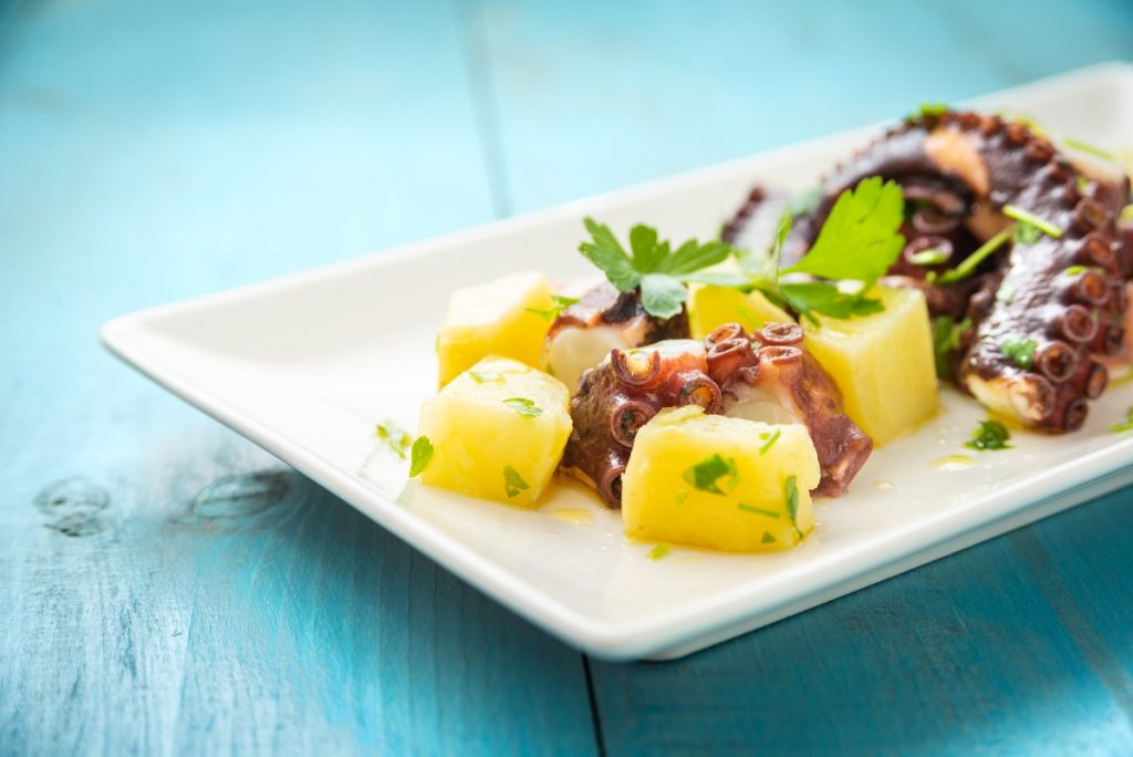 Insalata tiepida di polpo con patate: ricetta e video ricetta 3 polpo con patate: su tavolo azzurro piatto bianco con insalata di polpo con patate