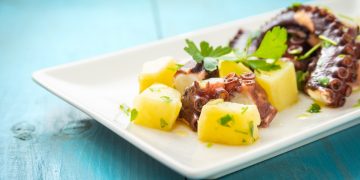 polpo con patate: su tavolo azzurro piatto bianco con insalata di polpo con patate