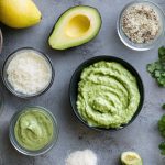 su tavolo di marmo, ciotola con la maionese di avovado e attorno tutti ingredienti limone, avocado tagliato in 2 limone, sale, erbe aromatiche