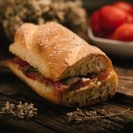 in primo piano il pane cunzato siciliano condito con pomodori freschi, acciughe, origano e un filo d’olio extravergine