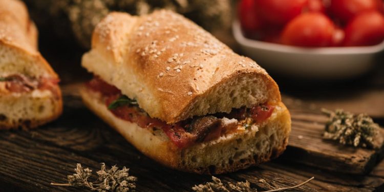 in primo piano il pane cunzato siciliano condito con pomodori freschi, acciughe, origano e un filo d’olio extravergine