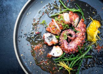 primo piano di un piatto nero con polpo cotto e tagliato con erbe aromatiche e fette di limone: ricette con polpo deliziose