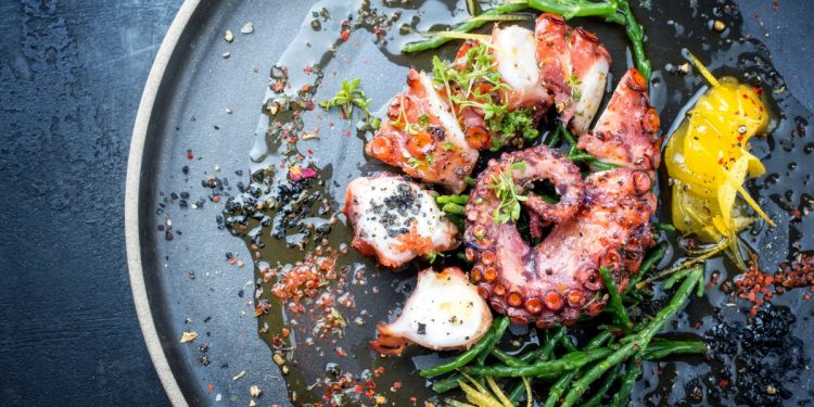 primo piano di un piatto nero con polpo cotto e tagliato con erbe aromatiche e fette di limone: ricette con polpo deliziose