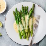 su piano da cucina di marmo piatto bianco con asparagi e salsa olandese accanto limone tagliato e ciotola con salsa