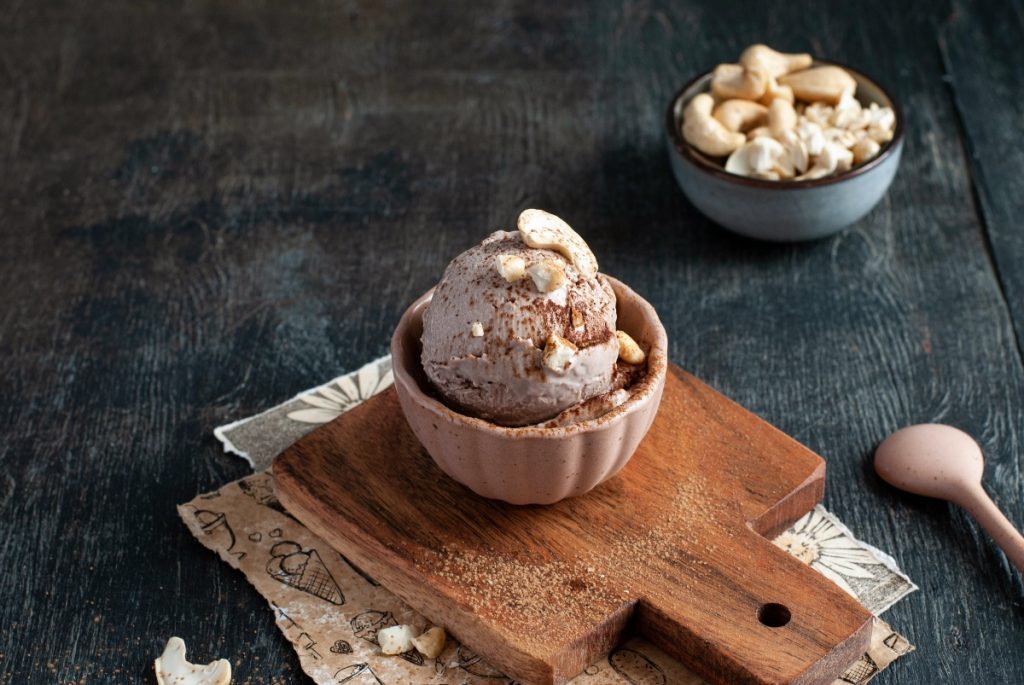 su tavolo di marmo tagliere con ciotola e una gelato senza lattosio con granella di cioccolato e mandorle, dietro ciottola con frutta secca