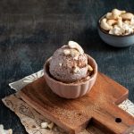 su tavolo di marmo tagliere con ciotola e una gelato senza lattosio con granella di cioccolato e mandorle, dietro ciottola con frutta secca
