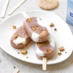 su sfondo bianco, piatto bianco  con gelato senza zuccheri aggiunti  fatto con i biscotti Céréal senza zuccheri aggiunti. Attorno bastono per gelati  e pezzi di biscotti