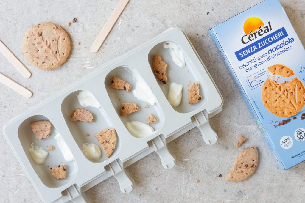 Una forma per 4 gelati a stecco, con dentro alcuni biscotti sbriciolati. Accanto una confezione di biscotti senza zuccheri Céréal