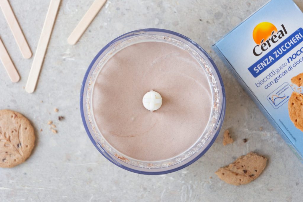 una ciotola tonda con la crema per il gelato dentro, accanto i bastoncini e una confezione di biscotti Céréal