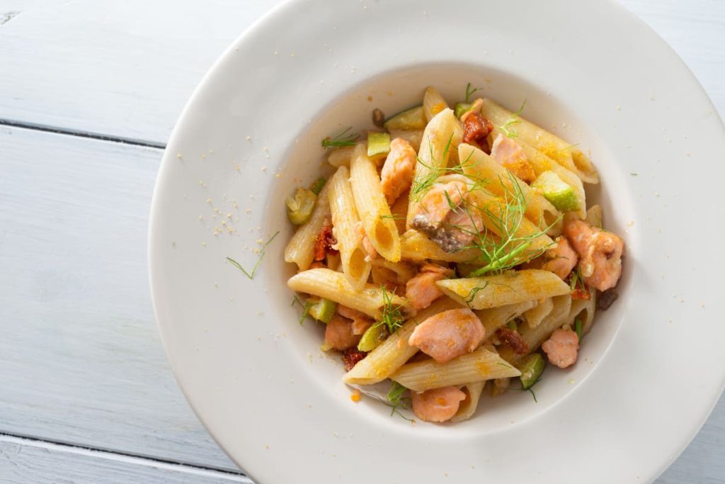 su base chiara una scodella bianca con della pasta zucchine e salmone