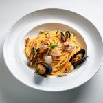 In primo piano su uno sfondo bianco c'è un piatto di spaghetti allo scoglio con frutti di mare come vongole e cozze.