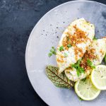Calamari gratinati al forno con pangrattato croccante, serviti con fette di limone e foglie verdi su un piatto grigio.