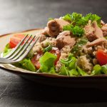 primo piano di un piatto sul tavolo con cous cous estivo con tonno, rucola, pomodorini e erbe aromatiche