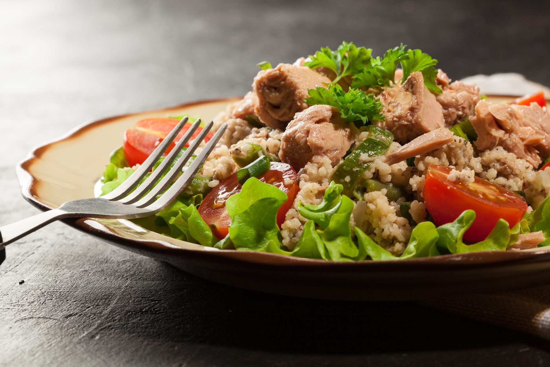 primo piano di un piatto sul tavolo con cous cous estivo con tonno, rucola, pomodorini e erbe aromatiche