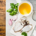 su tavolo di legno, tagliere di marmo con in una ciottola il fumetto di pesce, erbe aromatiche, cipolle e lische di pesce