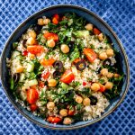 ricette con cous cous: su sfondo blu una ciotola con insalata di cous cous e ceci, pomodorini, olive nere e insalata