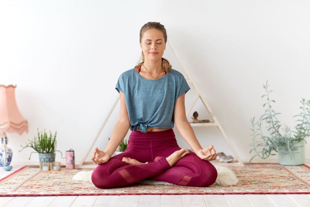 Donna in posizione di meditazione a gambe incrociate che pratica mindful eating e consapevolezza del respiro in un ambiente domestico.