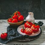 su tavolo di legno bianco piatto con canovaccio nero a righe bianche e un piatto con pomodori ripieni di tonno in scatola, dietro ciottola con pomodori e dietro una brocca d'acqua bianca su sfondo nero