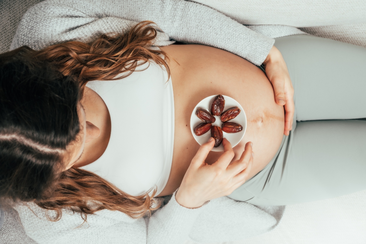 foto ripresa dall'alto di una donna incinta con la pancia che appoggia un piatto bianco con datteri per combattere acido folico basso