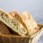 in primo piano delle fette di focaccia genovese appena sfornata, con impasto morbido e alveolato e una crosta dorata e fragrante, disposte in un cestino di vimini.