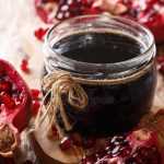 su tavolo di legno vasetto con marmellata di melograno e accanto melograna tagliata in 2