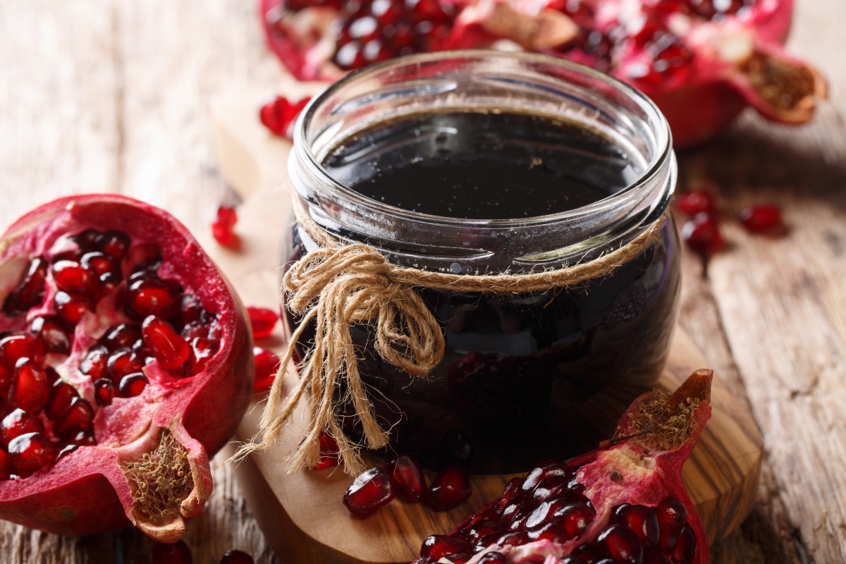 su tavolo di legno vasetto con marmellata di melograno e accanto melograna tagliata in 2