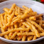 pesto alla trapanese: su tavolo di legno, primo piatto viola con pasta alla Trapanese e dietro pomodorini