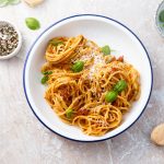 su tavolo di marmo, piatto bianco con bordo blu spaghetti con pesto alla siciliana e accanto pepe nero in una ciotola e un altra ciotola con sale e foglie di basilico