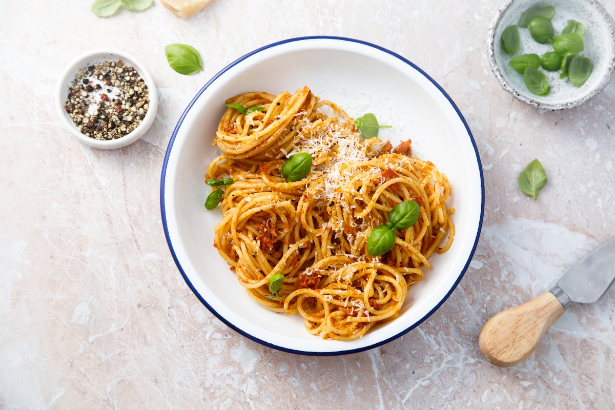 su tavolo di marmo, piatto bianco con bordo blu spaghetti con pesto alla siciliana e accanto pepe nero in una ciotola e un altra ciotola con sale e foglie di basilico