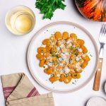Piatto di gnocchi di zucca conditi con parmigiano e prezzemolo su sfondo chiaro.