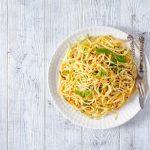 In primo piano un piatto di pasta alla carrettiera servito in un piatto bianco con erbe fresche e peperoncino su sfondo in legno chiaro.