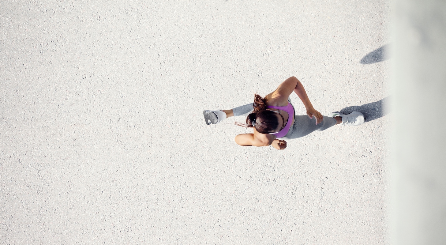 visto dall'alto una donna sta correndo su l'asfalto e durante la fase di volo alza il piede sinistro e si vedono il dorso delle scarpe running