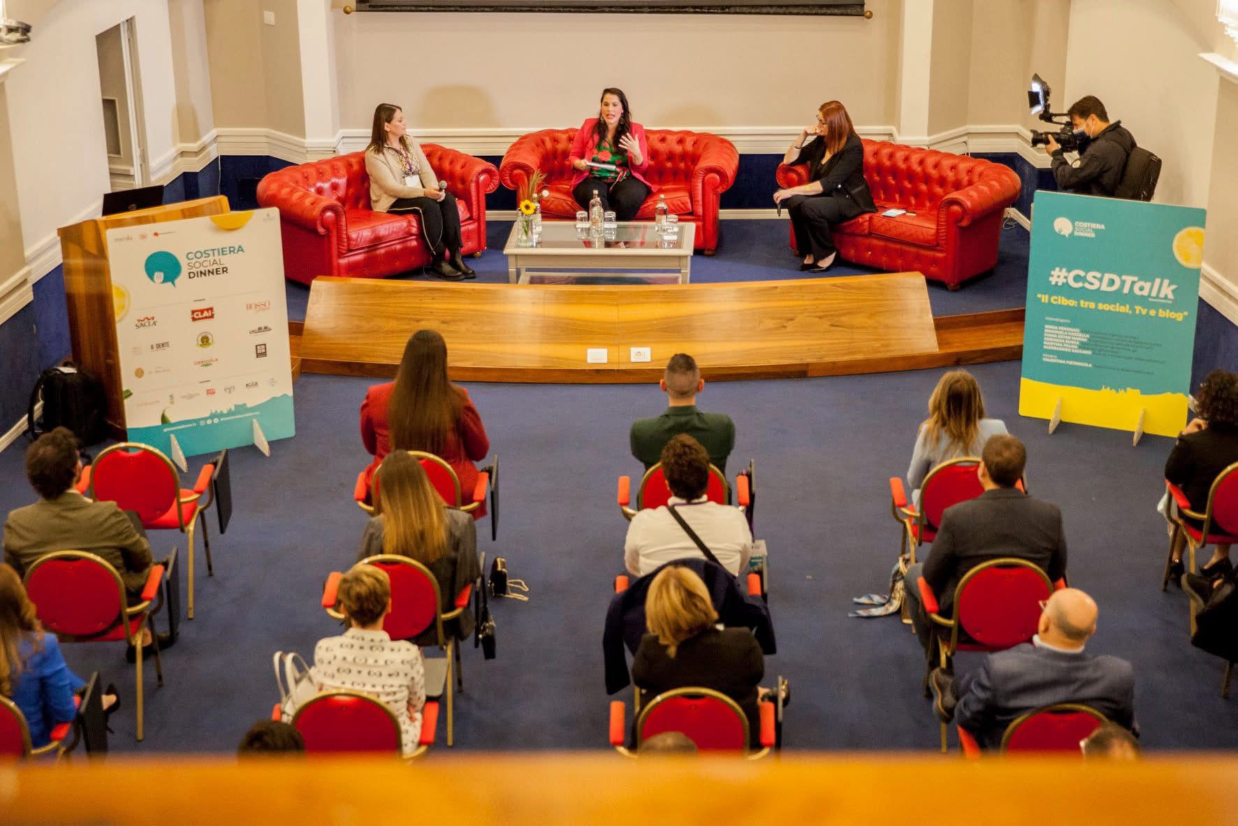 una sala con divani per i relatori e sedie per il pubblico