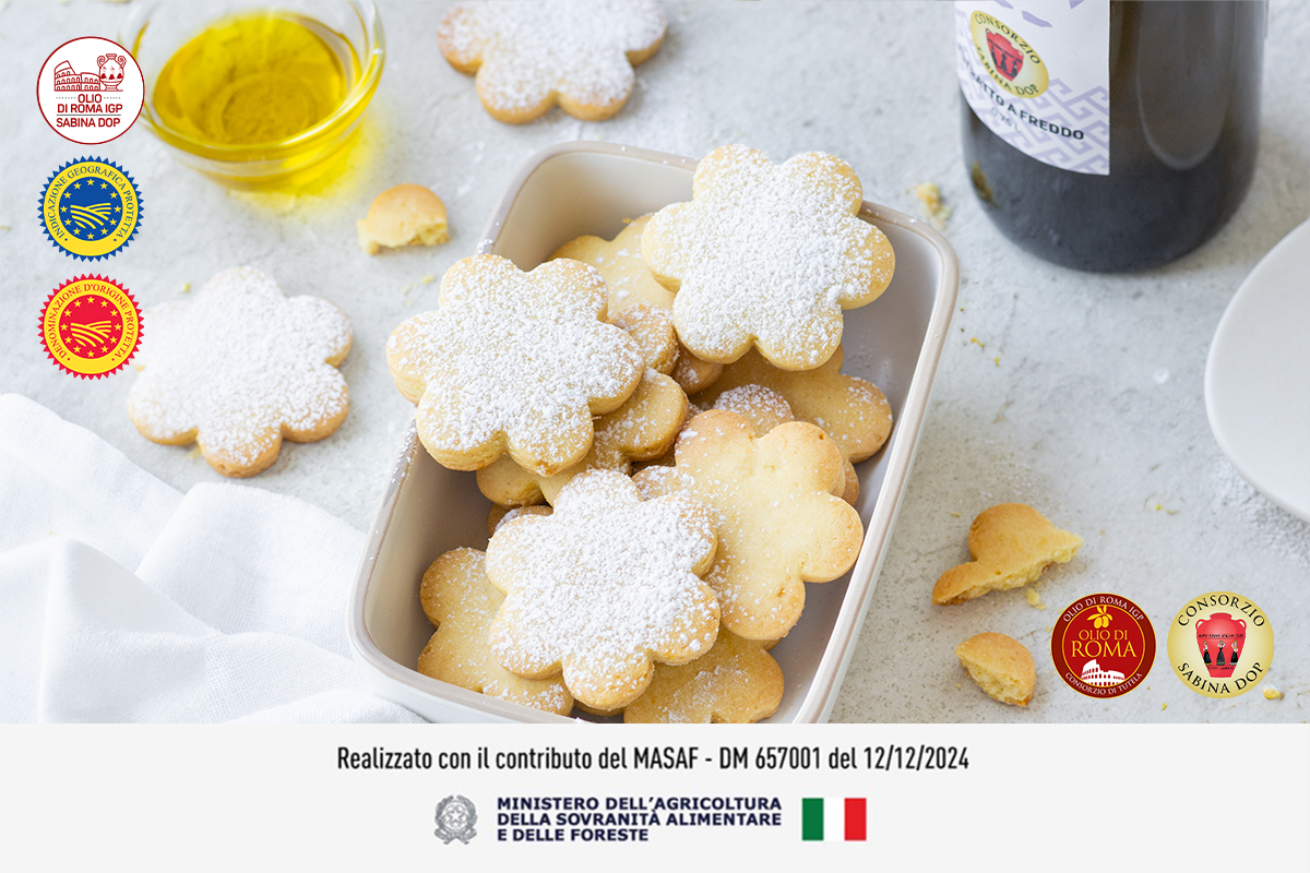 su tavolo, in un contenitore bianco di plastica, biscotti all'olio d'oliva, vicino biscotti sbriciolati, un contenitore con olio EVO. In alto a sinistra loghi dell'olio IGP e anche in basso a destra