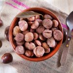 Castagne bollite: procedura, tempi di cottura e consigli di preparazione 1 su tavolo da cucina, canovaccio bianco a righe rosse, con una ciotola di terra cotta e castagne bollite sulla destra un cucchiaino di legno