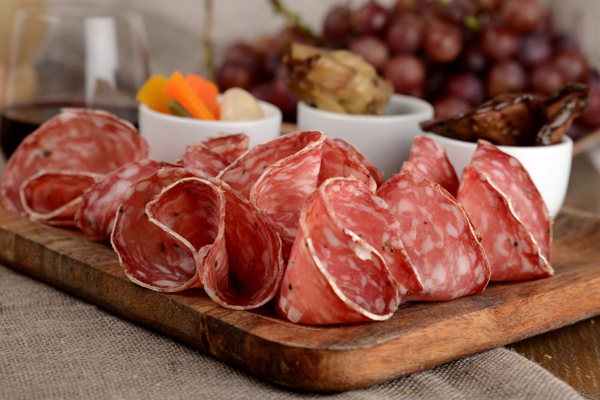 su un tagliere di legno tante fete di finocchiona e tre ciotole bianche per un aperitivo
