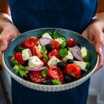 una donna tiene in mano un' insalatiera blu con una bella insalata mista con pomodori oli formaggio e cipolle