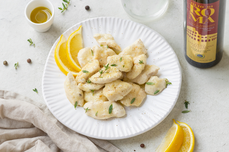 Pollo al limone in padella, un secondo leggero e saporito 6 In primo piano su una tavola bianca, c'è un piatto bianco con del pollo al limone e sulla destra una bottiglia di Olio di Roma IGP.
