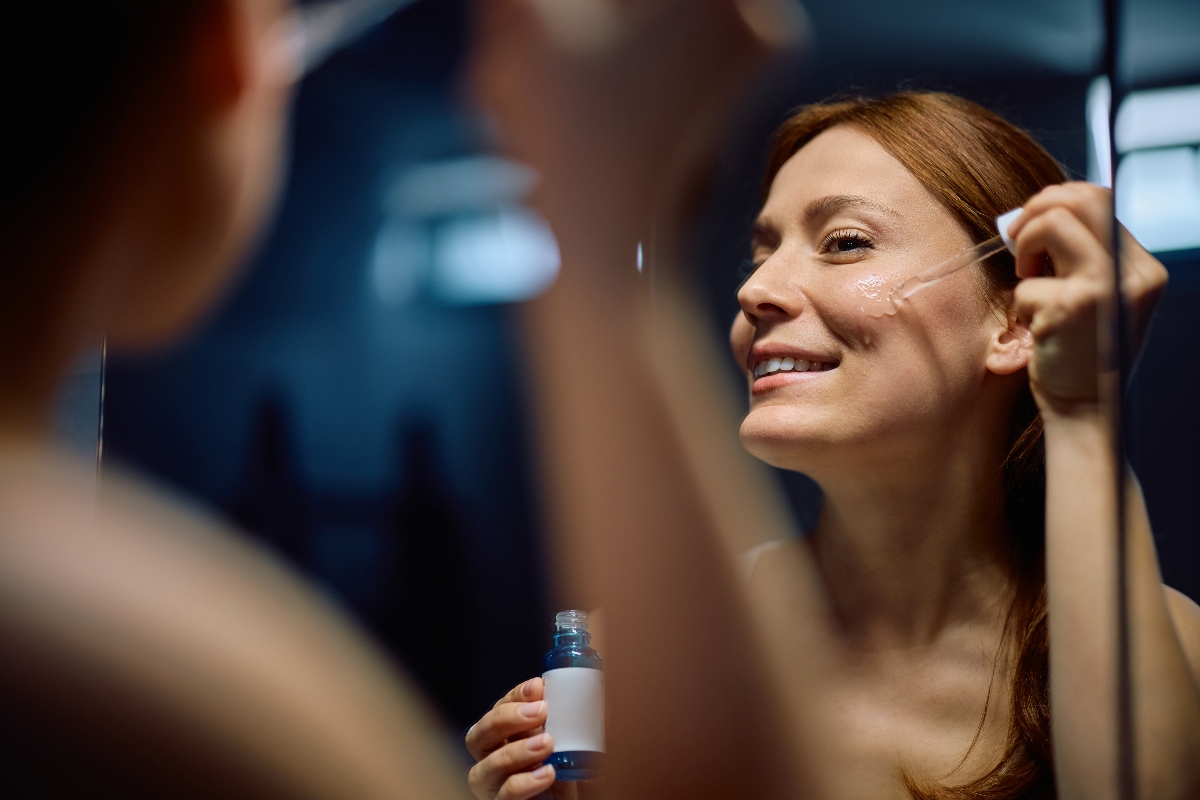una donna in bagno davanti allo specchio la sera usi un siero con retinolo per avere una pelle luminosa