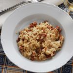 Riso alla pilota servito in un piatto bianco con salamella mantovana e grana grattugiato sullo sfondo.