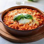 Riso alla pizzaiola: un primo piatto semplice, sano e delizioso 1 primo piano di un piano da cucina con un tagliere e un tegamino in terracotta con riso alla pizzaiola e mozzarella