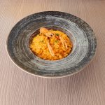 Risotto alla crema di scampi cremoso e senza panna 1 Piatto di risotto alla crema di scampi servito in un piatto fondo grigio su un tavolo di legno chiaro, con decorazione di prezzemolo fresco.