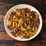 su tavolo di legno scuro piatto bianco con la pasta con sugo alla Genovese con cipolle e carne