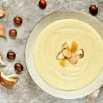 su piano di lavoro da cucina piatto fondo con una zuppa di castagne, attorno castagne e funghi