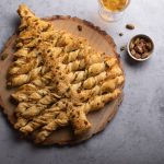 Albero di Natale di pasta sfoglia: video ricetta 1 In primo piano su un tavolo di marmo grigio, sopra un centro tavola in legno c'è un albero di natale di pasta sfoglia.