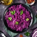 In primo piano su uno sfondo scuro, un piatto di cavolo rosso stufato in padella decorato con delle foglie di prezzemolo.