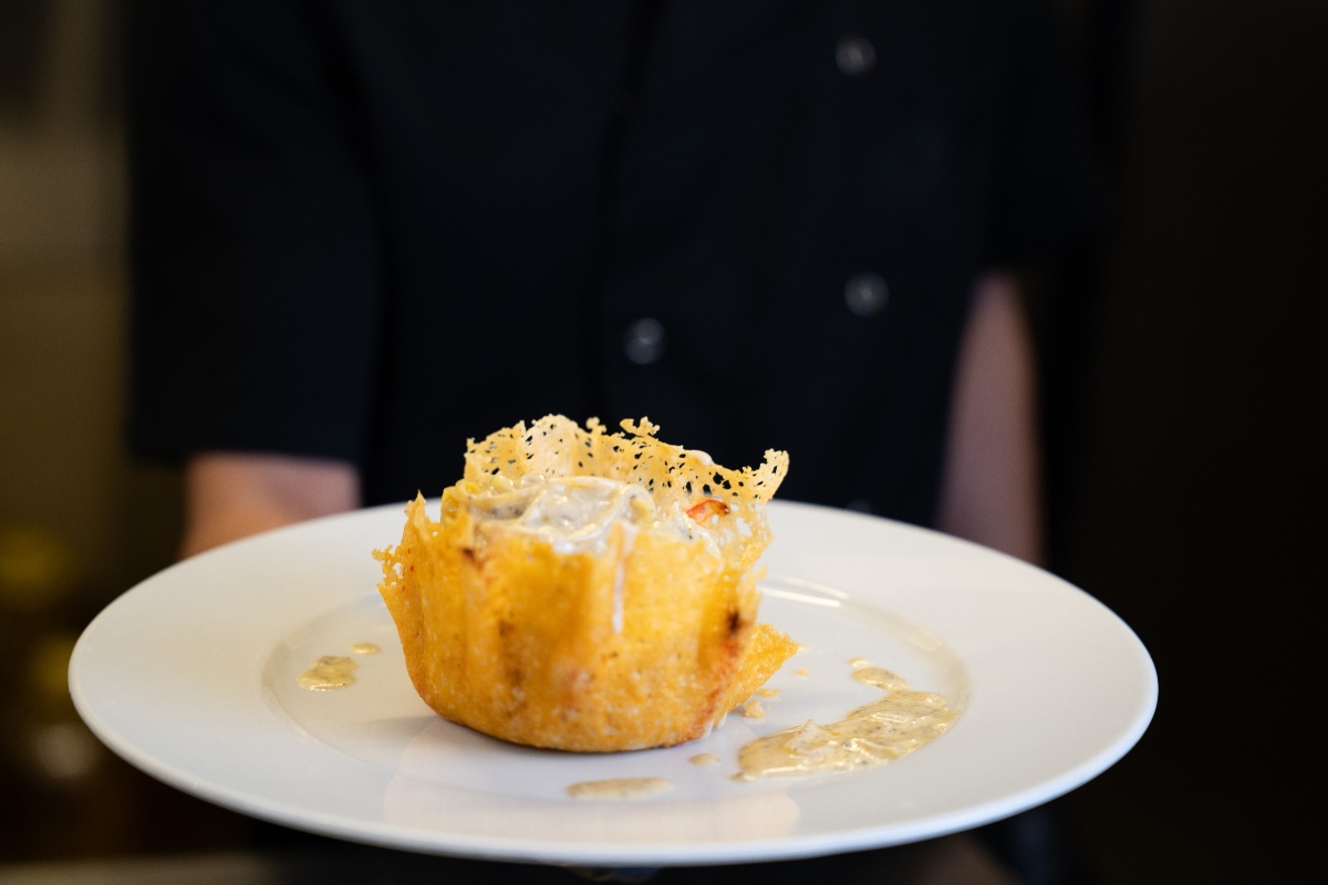 chef che tiene in mano un piatto bianco e presenta dei cestini di parmigiano con ripieni di formaggio